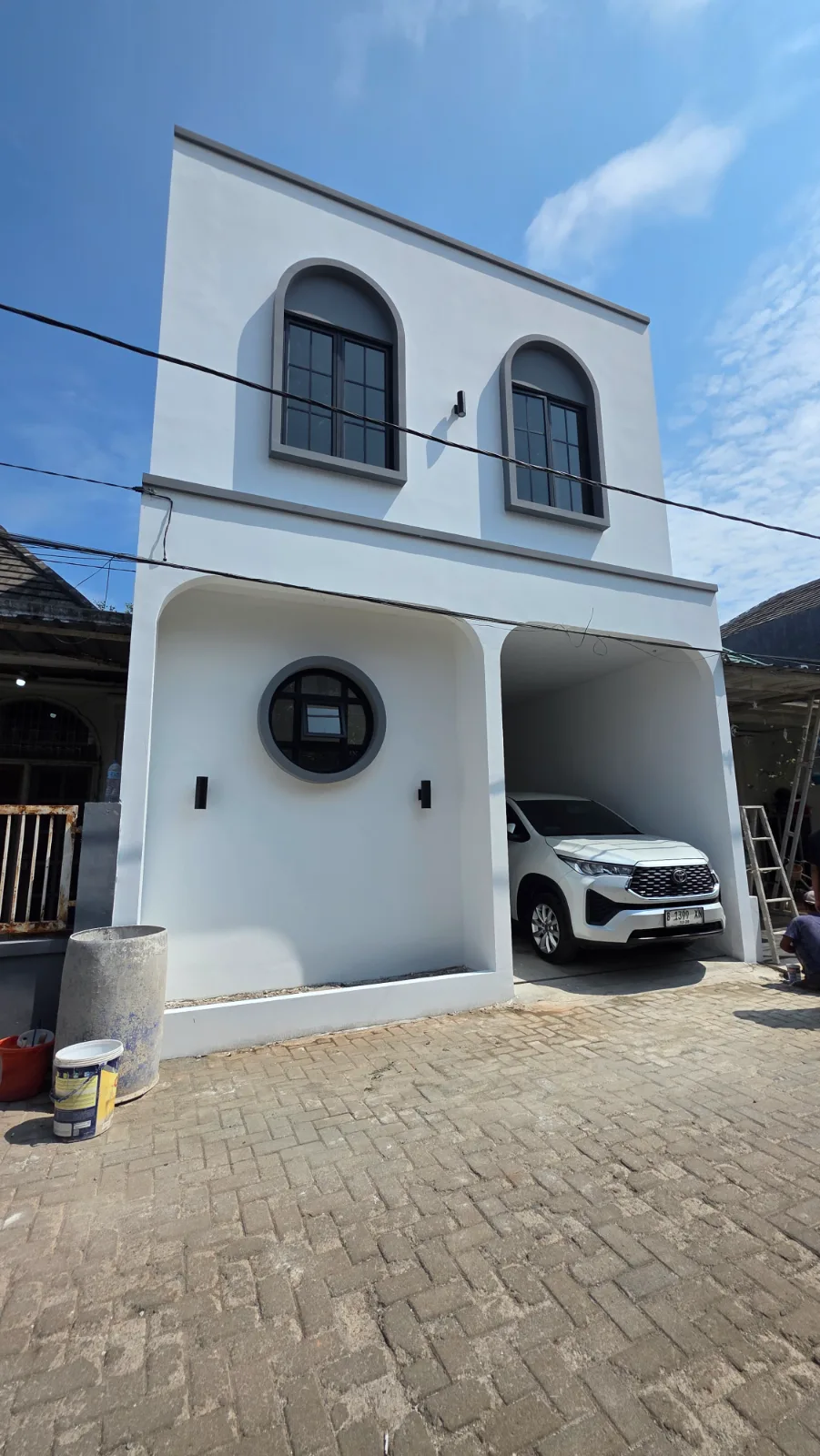 Detail fasad: jendela lengkung, jendela bulat, dinding putih bersih, dan carport mobil.